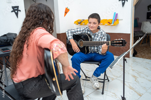 Young boy watching his guitar teacher closely while learning technique during a private lesson. Concept of focused learning, music education, and instrumental skill development