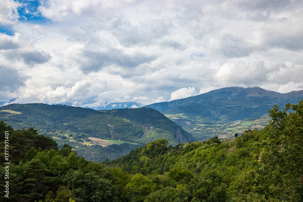 Fototapeta premium Green meadows and cloudy mountains on the road to La Salle-en-Beaumont in the Auvergne-Rhone-Alpes region, France