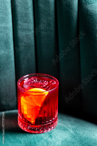 A classic Negroni cocktail with a large ice cube and an orange slice garnish in an old-fashioned glass on a dark velvet background.