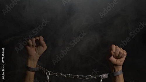 A man with hands bound in irons on a smoky black background