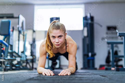 Focused woman doing plank exercise. Focused woman in plank position training core strength on gym floor.