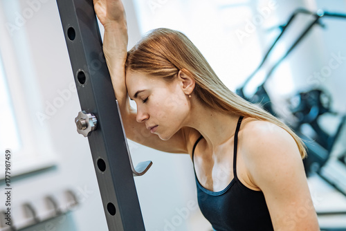 Tired woman resting during workout. Exhausted woman leaning on gym equipment while taking break after exercise.
