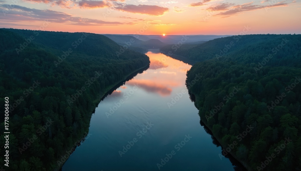 Obraz premium Aerial photo of a winding river surrounded by green forest. The setting sun reflects in calm water. Natural landscape presents a serene vista. Tranquil scene showcases peaceful atmosphere.