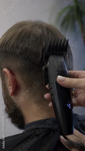 Barber wielding electric hair clipper making Fashionable haircut close up. Bearded Man client visit gentleman grooming beauty salon for hairstyle care. Modern Haircut style in barber shop 