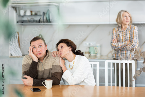 Kind woman asking livid middle-aged man for forgiveness during domestic quarrel in the kitchen