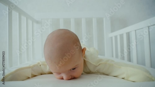 A small one-month-old baby is lying on its stomach in a crib and trying to lift its head. The concept of children's development
