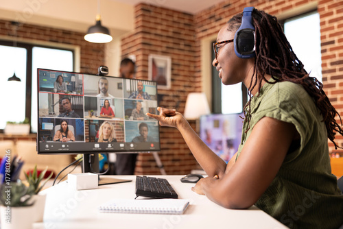 Fotografie Black female manager uses headphones and computer in communicating with colleagues during virtual meeting