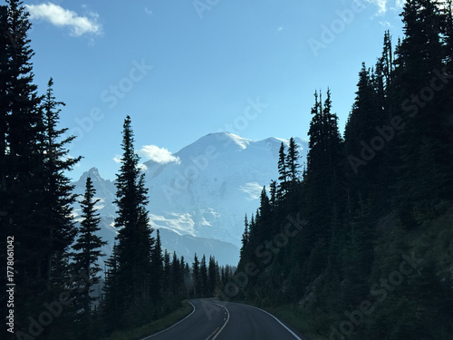 Glacier view framed by leafy trees in Mount Rainier National Park view from the windshield of a car with a long paved road.USA, Washington july 22 2025.