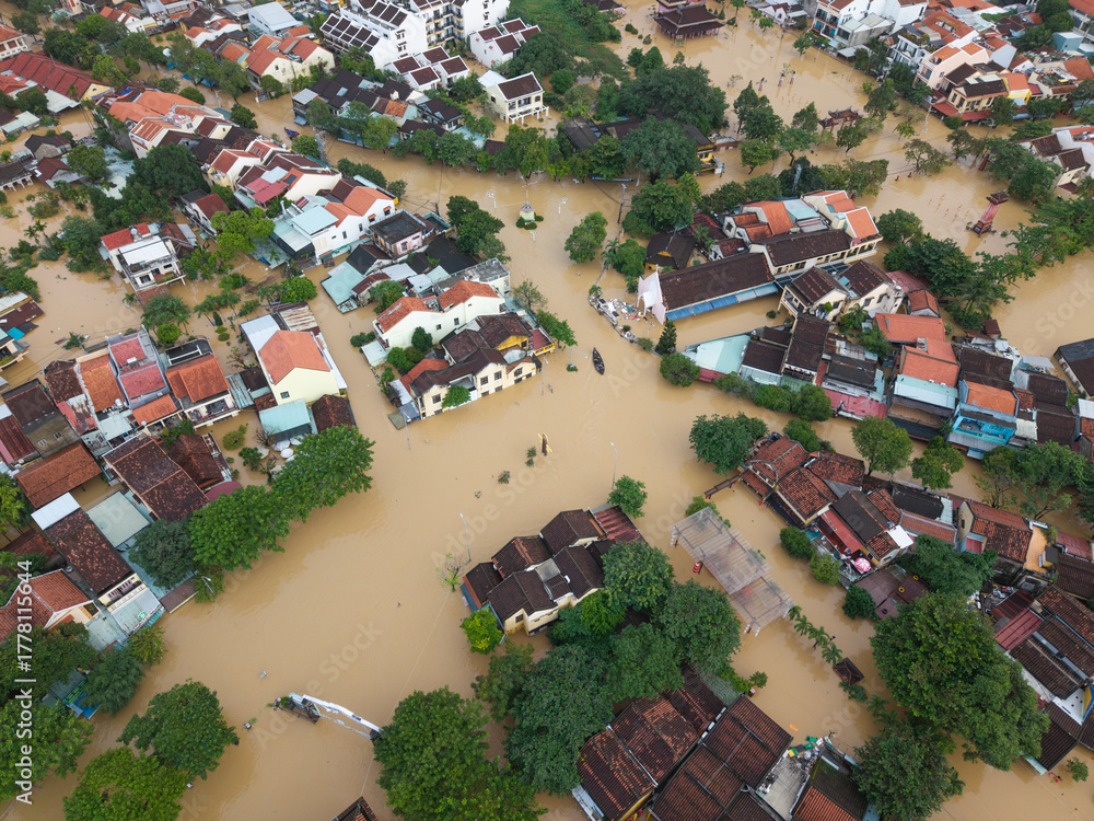 Fototapeta premium The deepest flood in history in Hoi An, Da Nang 2025. Aerial view of flooded ancient Asian town with yellow houses and brown roofs, showing severe urban flooding and climate disaster impact