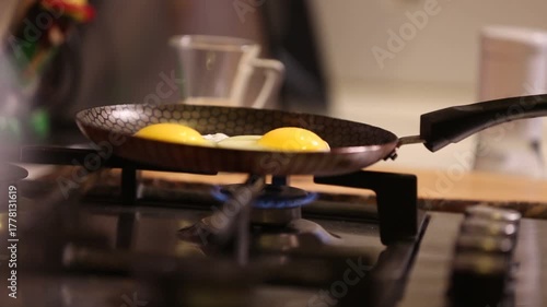 Fresh eggs are frying in a non-stick pan over a blue gas flame on a modern kitchen stove. Preparing a simple, delicious breakfast meal at home.