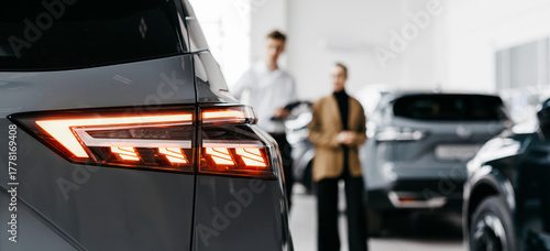 Modern car dealership interior showcasing sleek vehicle rear lights with customers discussing options in the background, emphasizing the car sales experience and customer engagement