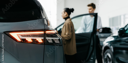 Modern car dealership interior featuring sleek vehicle design, illuminated taillights, and customers engaging in car sales discussions, showcasing a vibrant automotive sales environment