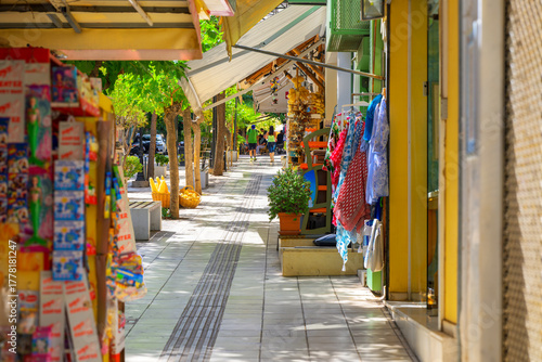 Fototapeta Naklejka Na Ścianę i Meble -  Colorful shops and sidewalk cafes line 28th of October street, a picturesque narrow pedestrian street at the seaside resort town of Agios Nikolaos, Greece, on the island of Crete.