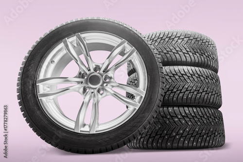 A tire shop showcases a set of four winter tires stacked beside an alloy wheel. These studded tires are designed for improved traction in winter conditions, perfect for safe driving.