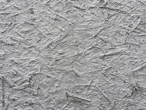 Close-up of a gray textured surface resembling rough plaster or concrete with embedded wood fibers, creating an abstract industrial pattern.
