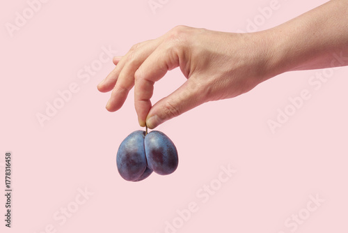 Female hand pinching plum on pink background