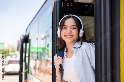Asian woman tourist holding bag strap while going out or getting off the shuttle bus at stop station