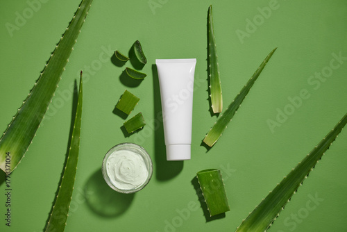 An eye-level shot of a cream tube, aloe vera leaves, and cream bowl