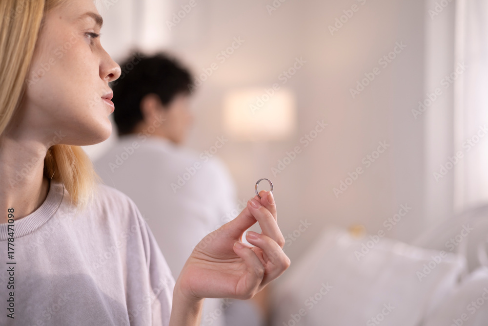 Fototapeta premium A couple is arguing in bed. The relationship is in trouble. The wife holds her wedding ring in disappointment and sorrow for her husband, which may lead to divorce. Family problems.