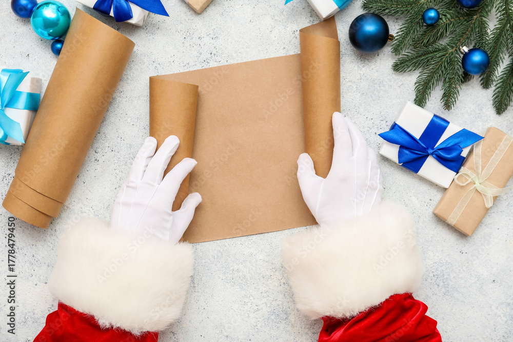 Obraz premium Santa hands with blank scroll, Christmas gifts and decorations on light background, closeup