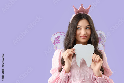 Young woman in fairy costume with paper tooth on lilac background