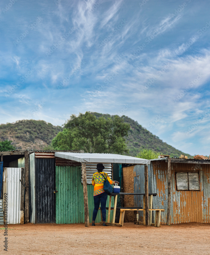 Fototapeta premium african woman worker going to work in the morning in the shanty town , south africa, shack made of corrugated sheet galvanized metal