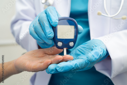 Asian doctor using digital glucose meter for check sample blood sugar level to treatment diabetes.