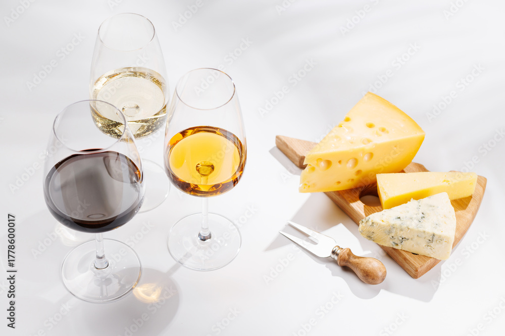 Fototapeta premium Assorted cheeses and wine glasses on white background