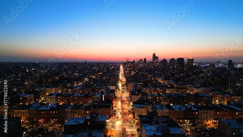 Aerial view of a city street at dusk, illuminated by vehicle and building lights