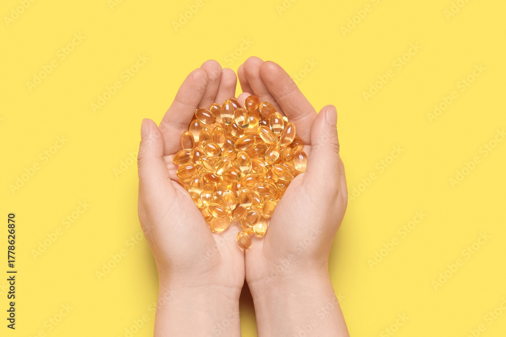 Obraz premium Female hands with vitamin E capsules on yellow background