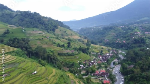 Stunning aerial view of a mountain valley with lush green rice terraces, a village, and a river.