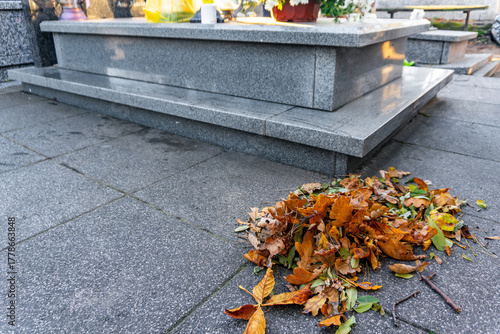 Pile of autumn leaves collected beside granite gravestone in cemetery, cleaned memorial area during seasonal maintenance on an autumn day