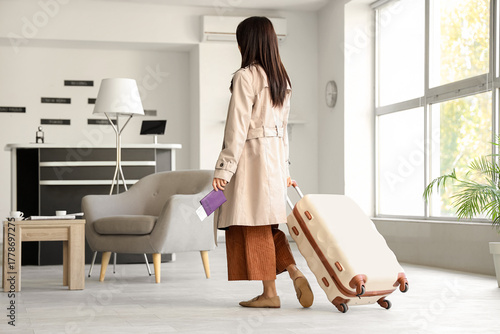 Young woman with passport and suitcase walking in airport lounge, back view