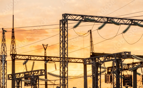 Sunset over power station with transmission towers and electrical equipment in silhouette