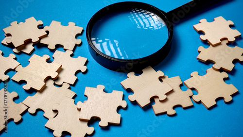 Obraz na płótnie Search for the Missing Piece: Magnifying Glass Inspecting Wooden Jigsaw Puzzle o
