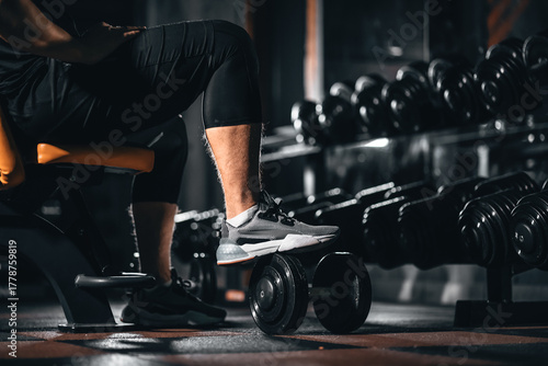 Male bodybuilder taking break during gym training with dumbbell, Man resting in sport gym showcasing bodybuilding lifestyle