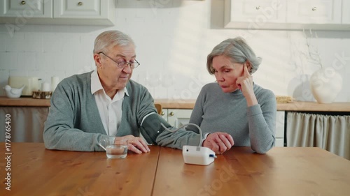 Aged man and woman using modern electronic monitor for measuring blood pressure. Healthcare and body condition control in old age, careful wife and sick man, risk of insult and heart attack after 60