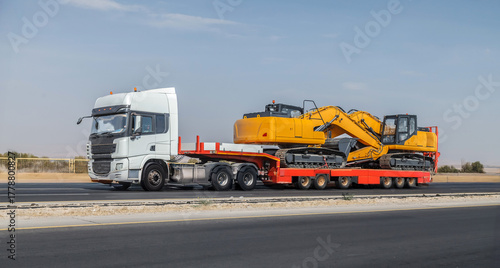 Large truck is pulling a trailer with a yellow and black machine on it