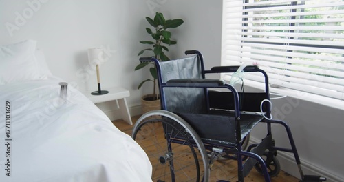 Displaying bedroom with wheelchair occupying center-right featuring bed nightstand lamp blinds