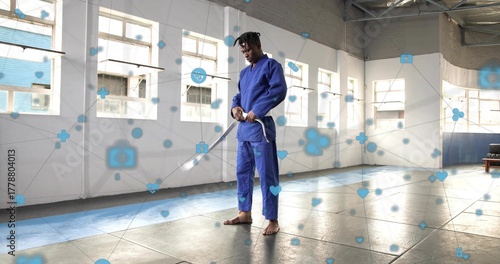 Adjusting stance martial artist wearing blue gi holding wooden sword in dojo, with digital overlay