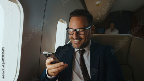 Fotografie Businessman smiling happily while watching content on his mobile phone, travelin