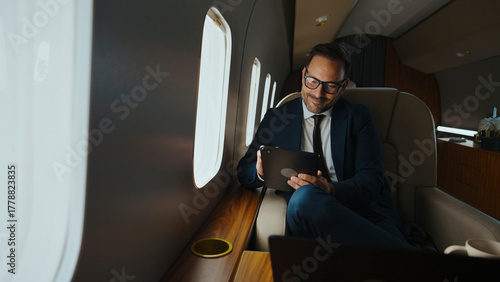 фотографія Businessman in suit traveling on a private jet, using a digital tablet for work,