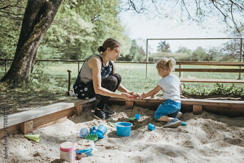 Mother playing with little daughter in sandbox on a playground