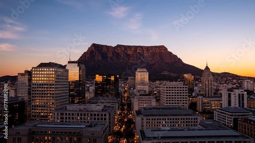 City skyline featuring skyscrapers and a prominent mountain at sunset, with golden light