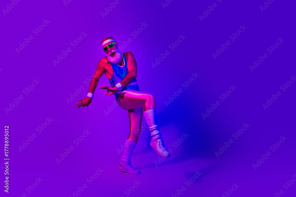 Fototapeta premium Dynamic retro fitness man jumps in neon purple blue studio wearing a jumpsuit and headband for a vibrant lifestyle image