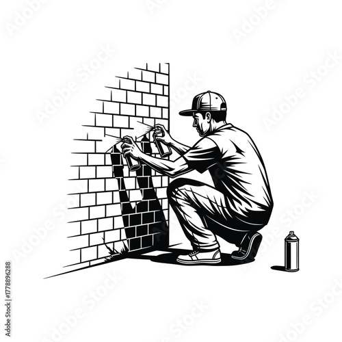 Graffiti artist in a baseball cap crouches down to spray paint on a brick wall with a spray can