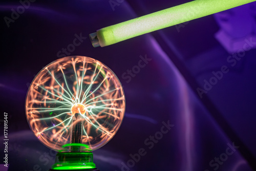 A fluorescent tube held near a plasma ball begins to glow. This physics experiment demonstrates wireless power transfer and the excitation of inert gas by a high-frequency field.