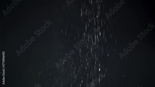 Abstract image of vertical flow, particles glistening against a dark background, suggestive of rain