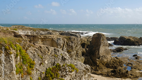 Fototapeta Naklejka Na Ścianę i Meble -  Rugged shoreline featuring weathered cliffs and large rock formations. Waves crash against rocky shore, creating dynamic and wild beauty. Atlantic coastline of Brittany, France.