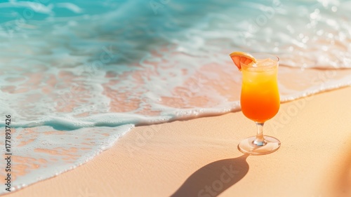 Orange and red tropical cocktail standing on beach near soft sea waves